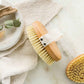 Oval dry brush with wood handle and yellow sisal bristle head, white fabric strap