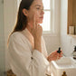 Woman applying Radiance Boosting serum, holding a small bottle with black dropper
