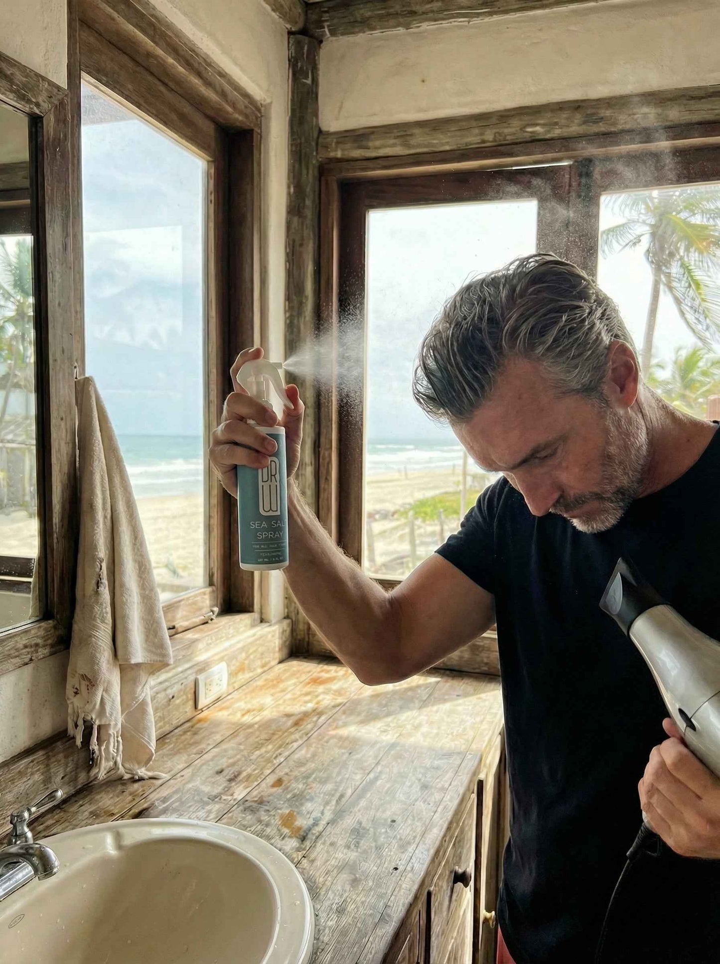 Sea salt spray bottle held near face with white trigger sprayer releasing mist