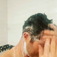 Shampoo foam on hair and shoulders, hands raised in shower