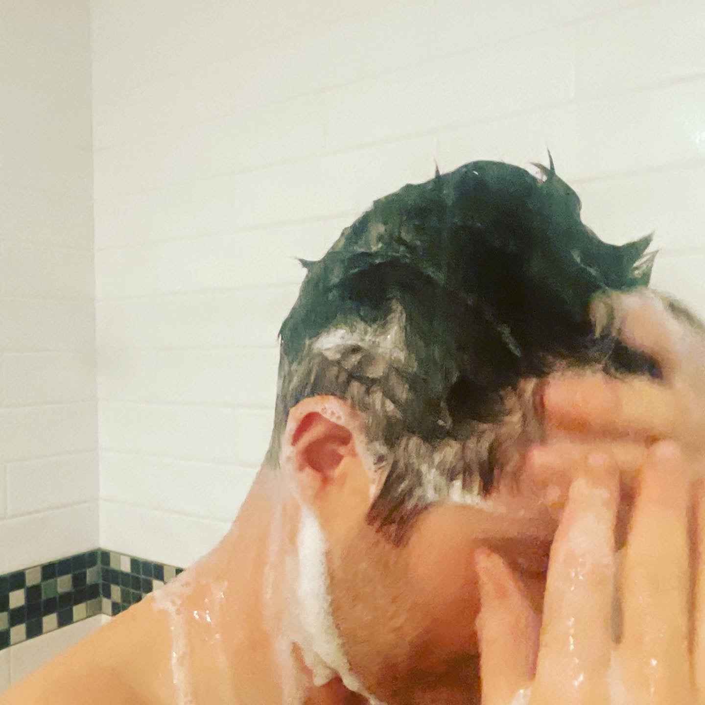 Shampoo foam on hair and shoulders, hands raised in shower